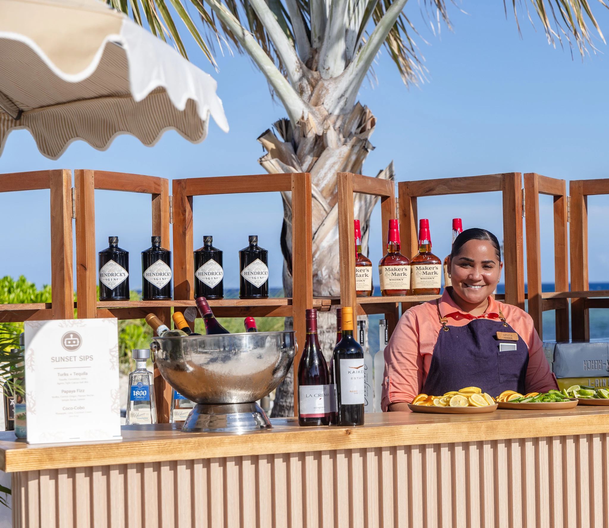 a woman behind a bar with bottles of wine and fruit