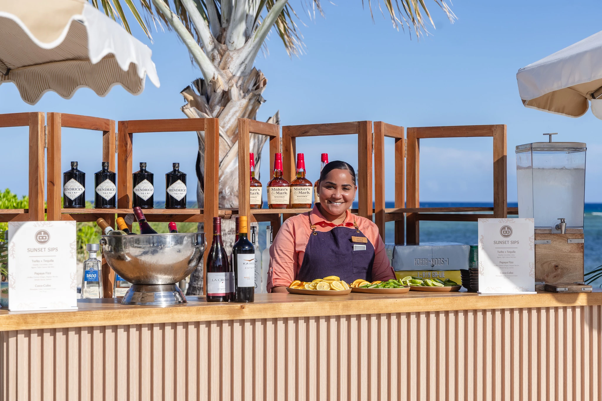 a woman behind a counter with bottles of wine and a palm tree