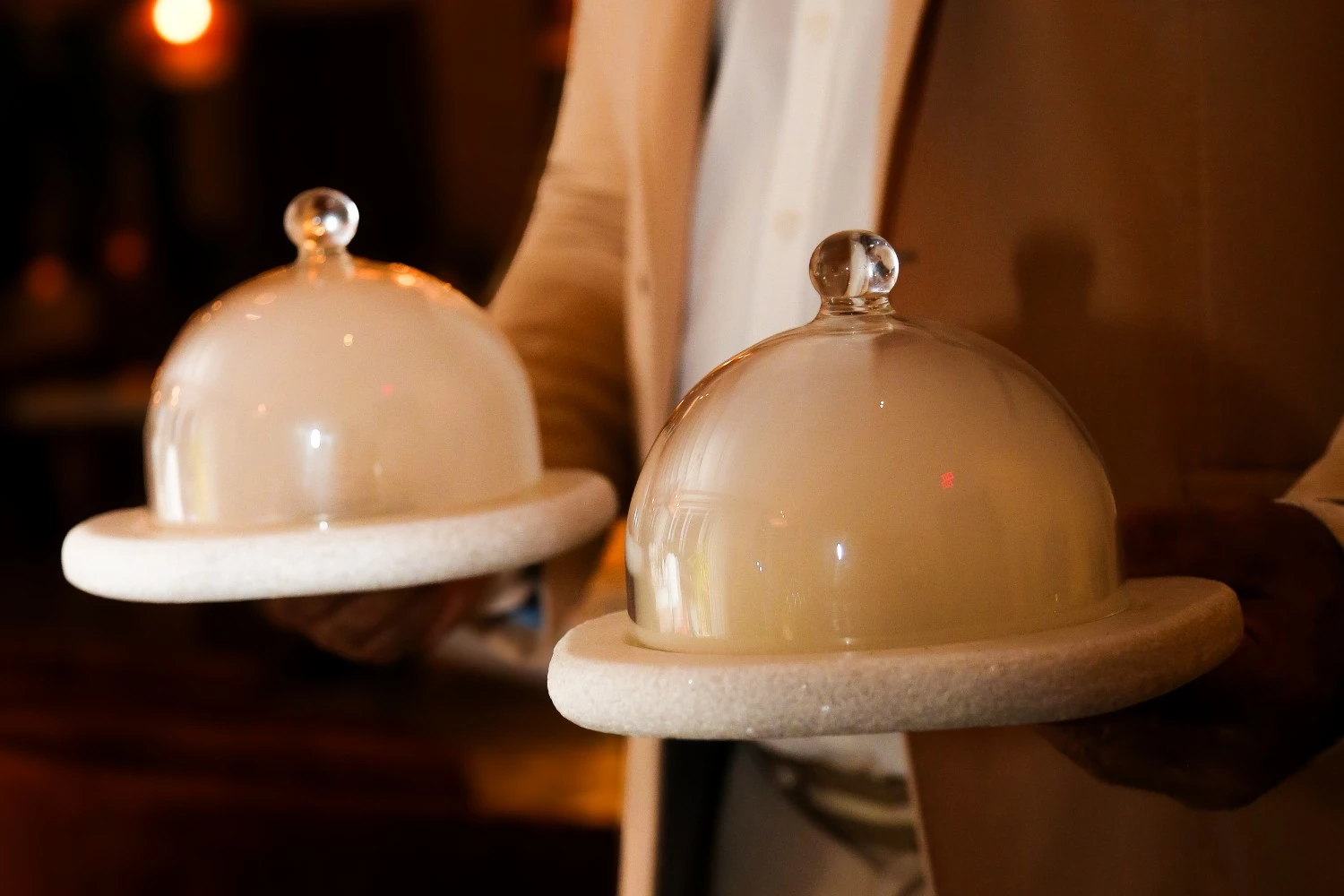 a person holding two trays with glass dome covers