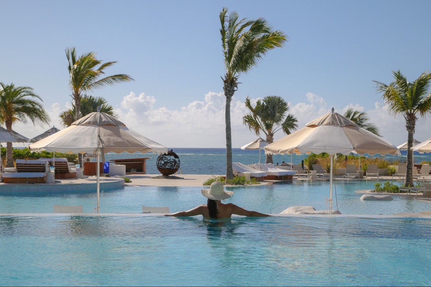 a woman in a pool with umbrellas and palm trees