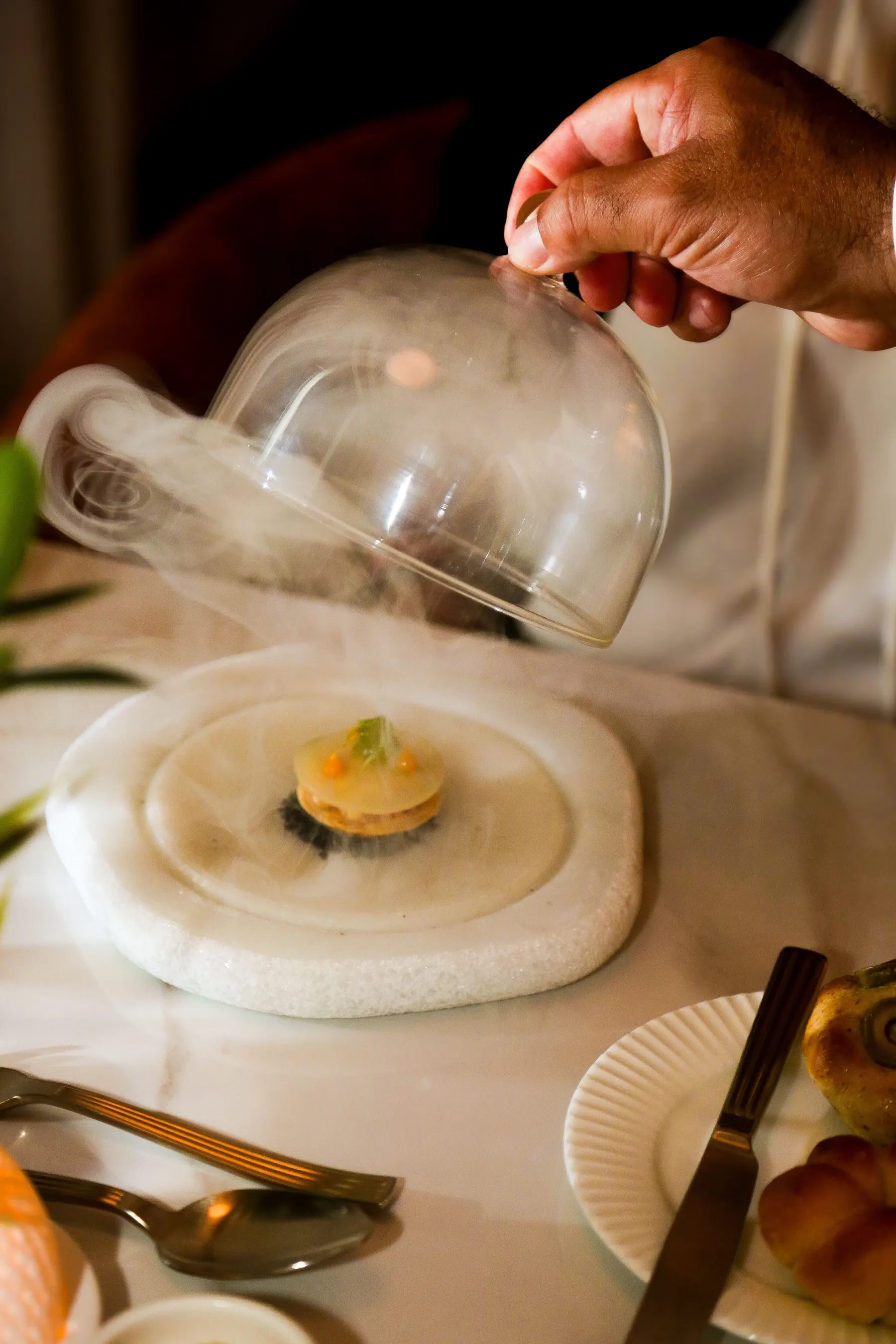 a hand holding a glass lid over a plate with food