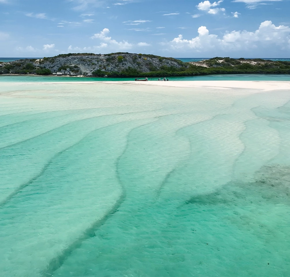 a clear blue water with a small island in the background