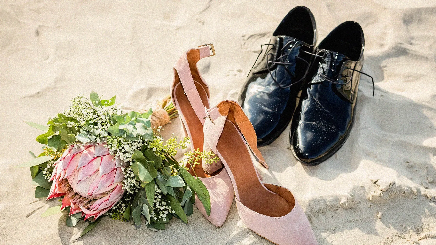 a pair of shoes and a bouquet of flowers on sand