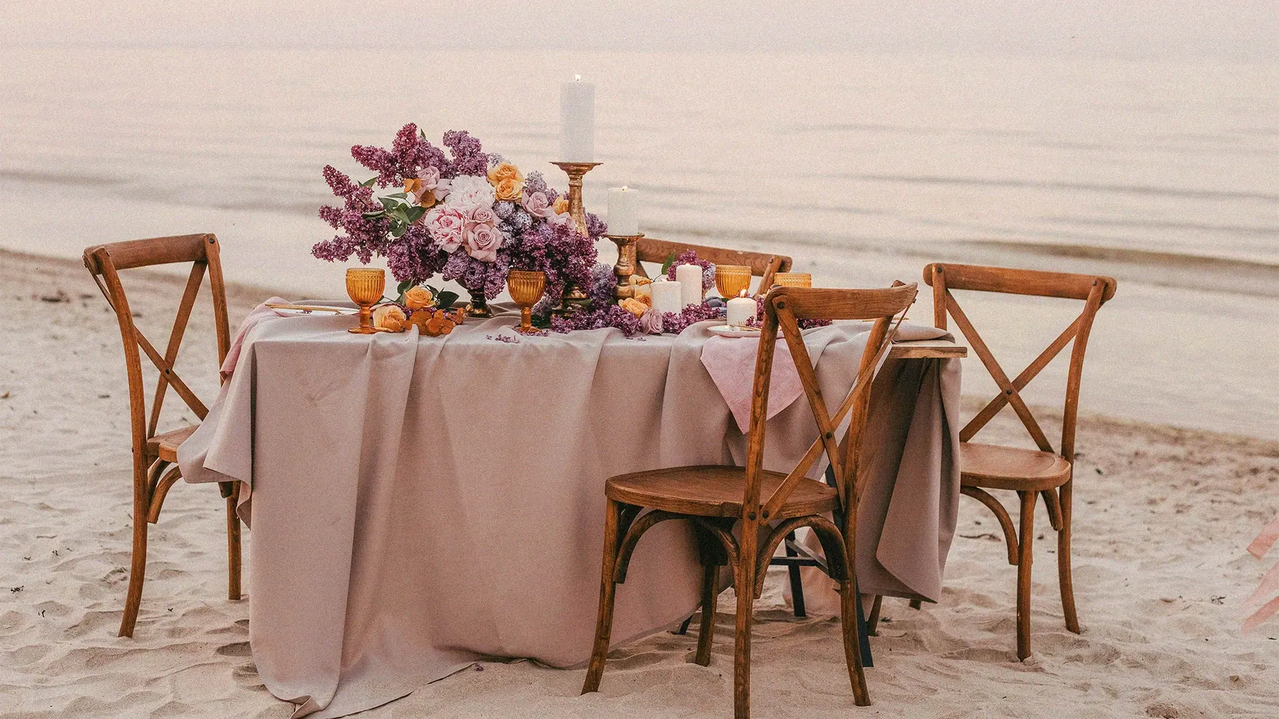 a table set up with flowers and candles on the beach