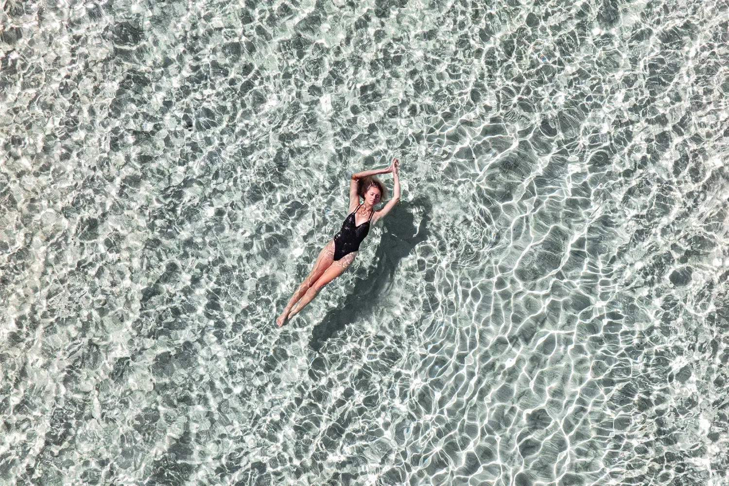 a woman in a black one piece swimsuit floating in clear water