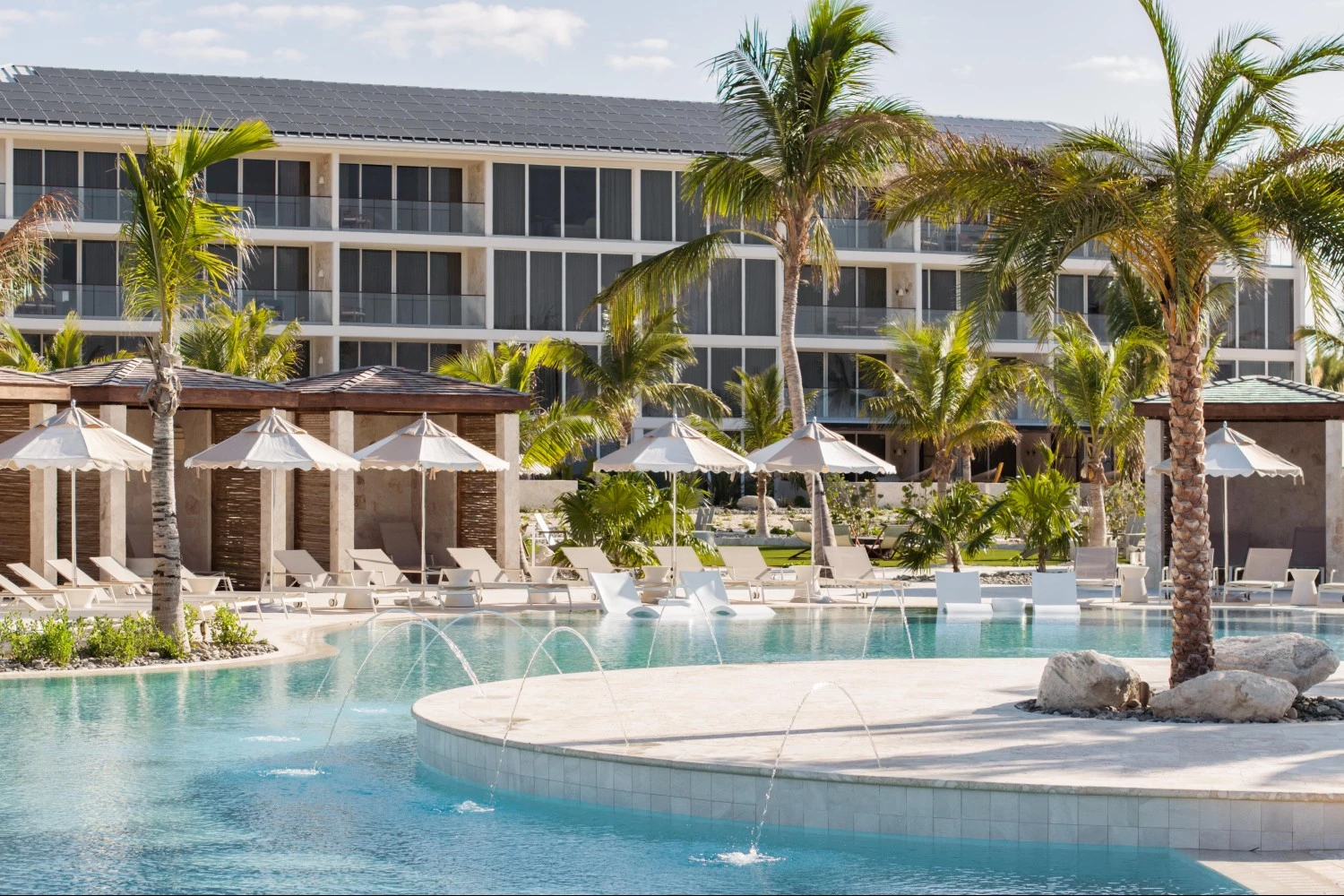 a pool with water jets and umbrellas in front of a building