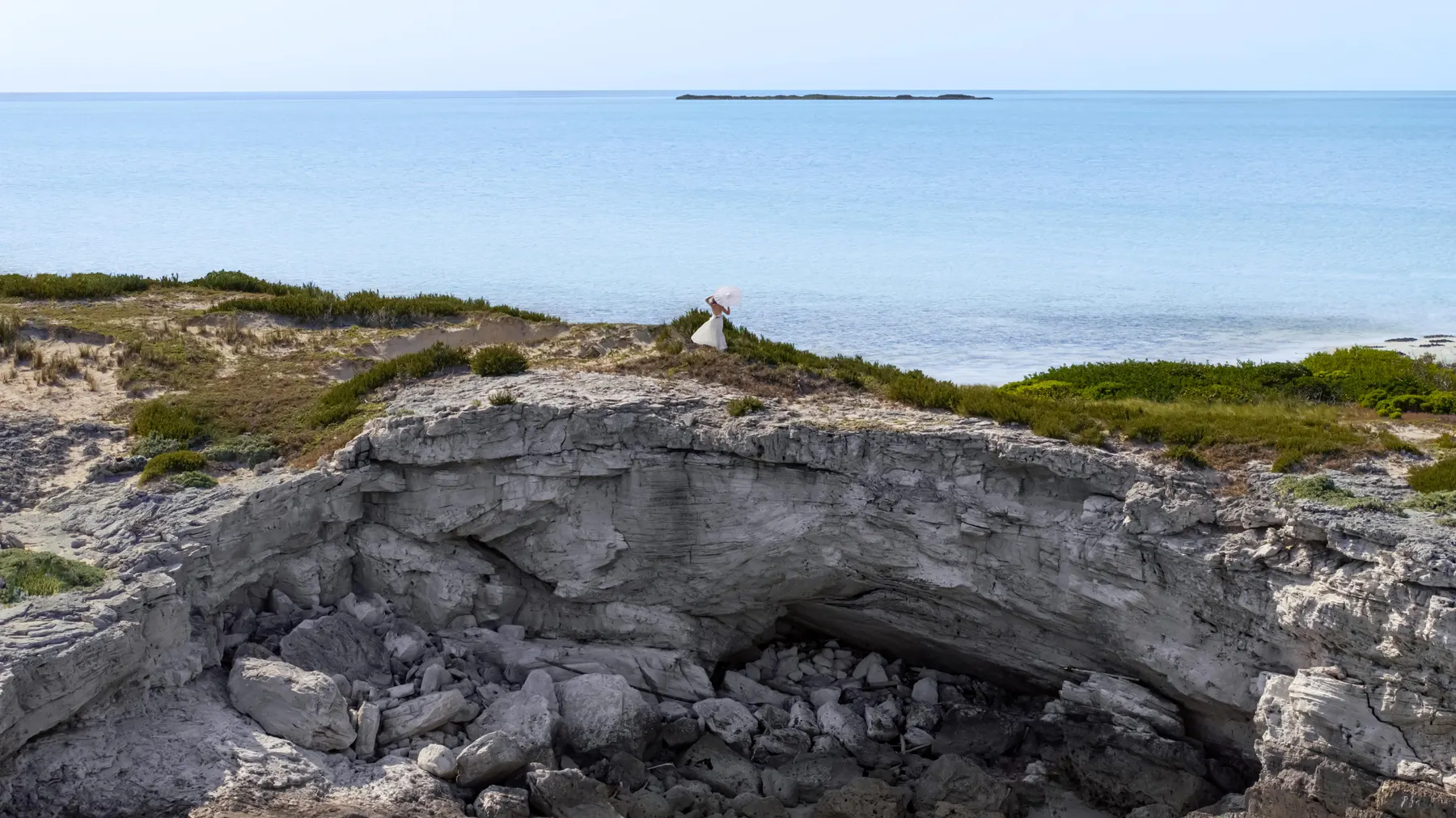 a woman in a white dress on a rocky cliff by the ocean