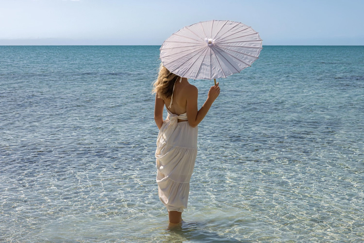 a woman in a white dress holding a white umbrella in the water